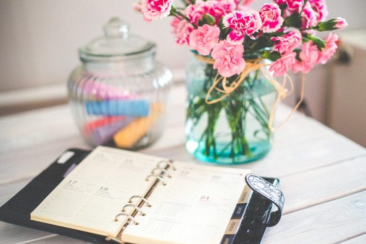 Agenda à anneaux ouvert sur une table blanche, à côté d'un bouquet de fleurs