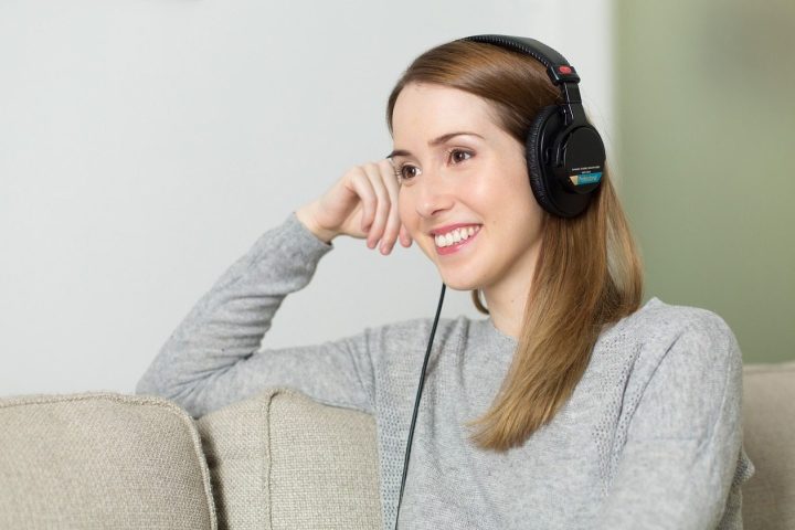 Une femme souriante écoute de l'audio dans un casque, assise sur un canapé