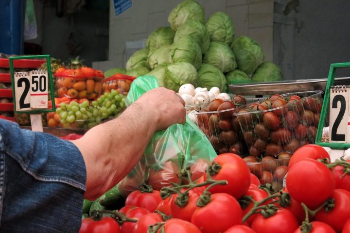 Main qui remplit un sachet de tomates fraîches à l'étal d'un marché