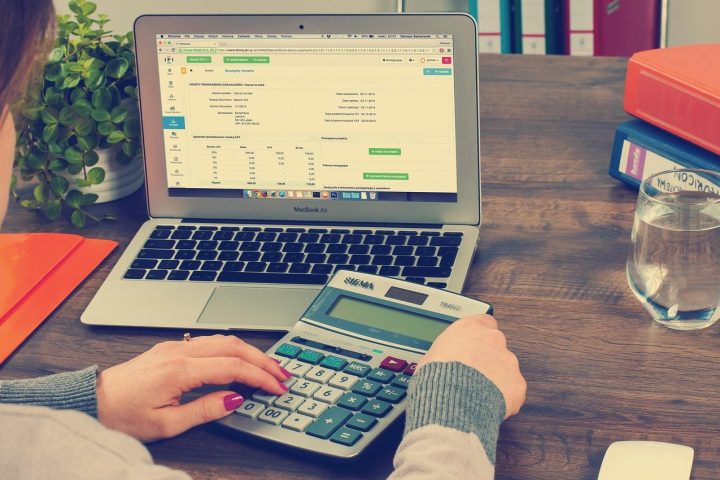 Une personne saisit des chiffres sur une calculatrice devant un ordinateur portable affichant un tableau
