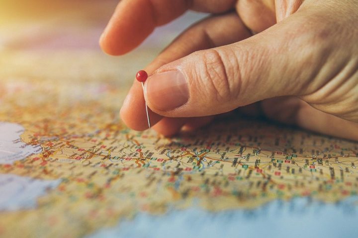 Une main plante une épingle rouge sur une carte géographique