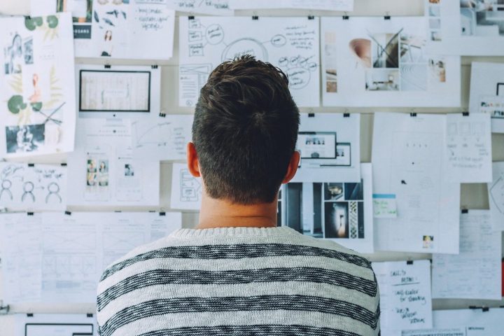 Homme de dos devant un mur couvert de feuilles de plans et de notes