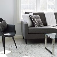 Petit salon clair avec canapé gris, fauteuil et table basse en verre