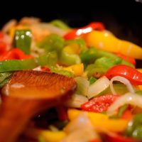 Poêlée de poivrons et d'oignons colorés remuée à la cuillère en bois
