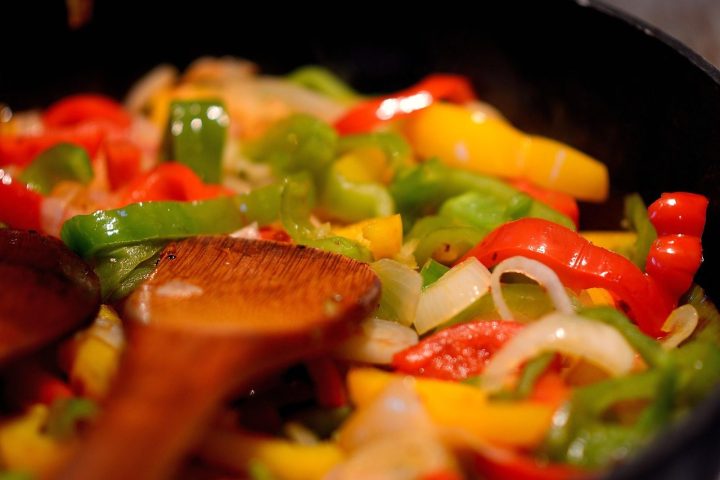 Poêlée de poivrons et d'oignons colorés remuée à la cuillère en bois
