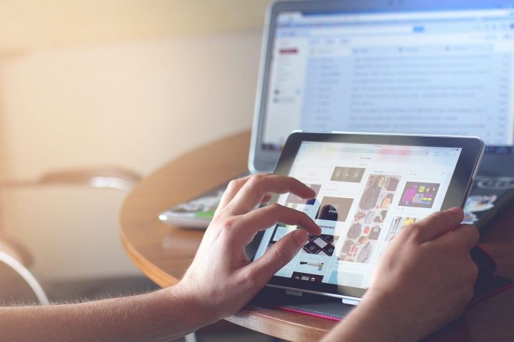 Mains qui utilisent une tablette posée sur une table devant un ordinateur