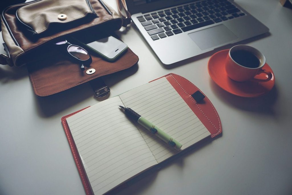 Carnet de notes ouvert avec un stylo, une tasse de café et un ordinateur portable sur un bureau