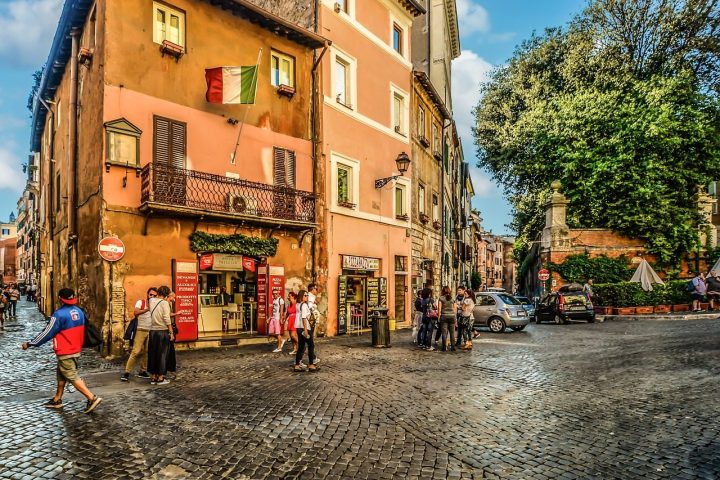 Rue pavée d'un quartier ancien en Italie, avec façades ocre, drapeau italien et passants