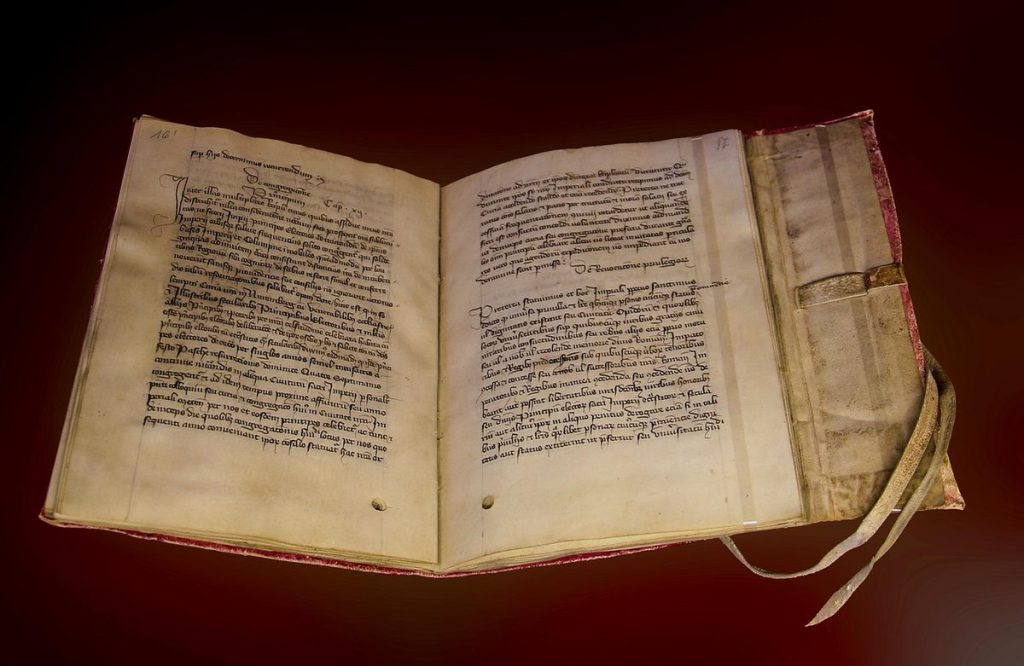 Manuscrit médiéval ancien en écriture latine, ouvert sur un fond sombre