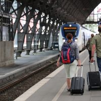 Deux voyageurs avec sacs à dos et valises à roulettes sur un quai de gare européenne, un train à l'arrêt devant eux