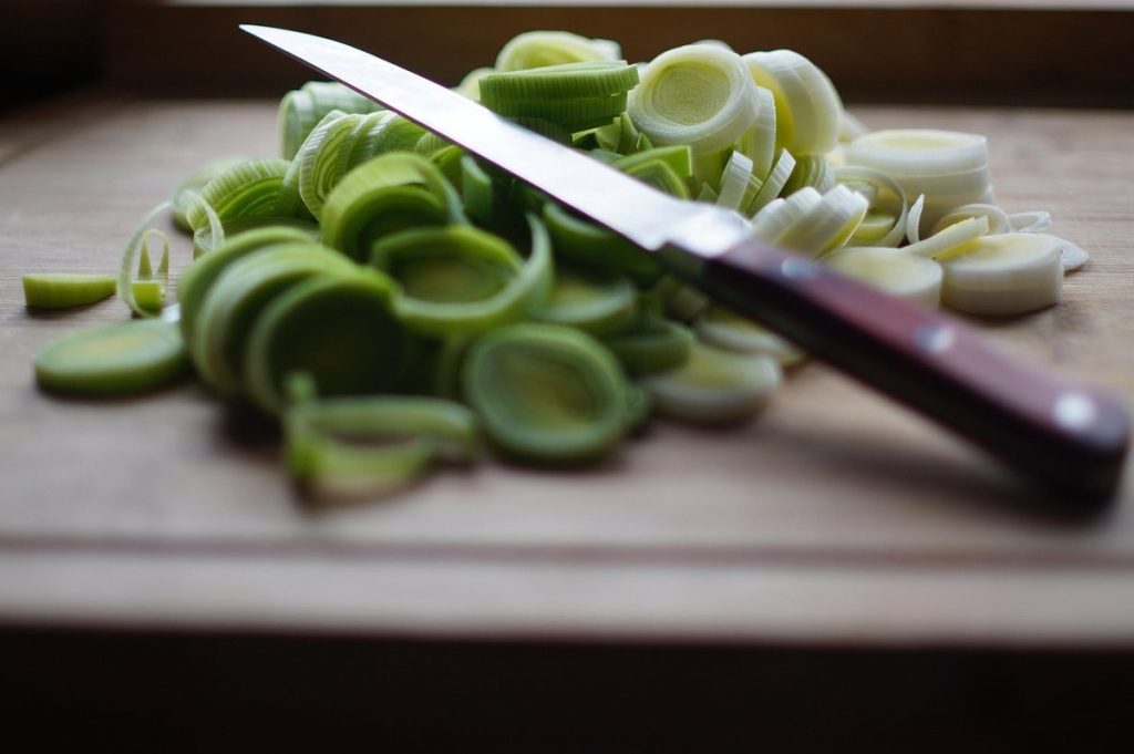 Couteau de chef posé sur une planche à découper en bois, au-dessus de poireaux émincés