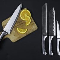 Couteau de chef, couteau à pain, couteau dentelé et couteau d'office sur fond noir, avec une planche à découper
