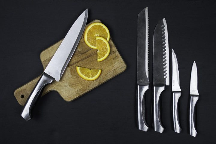 Couteau de chef, couteau à pain, couteau dentelé et couteau d'office sur fond noir, avec une planche à découper
