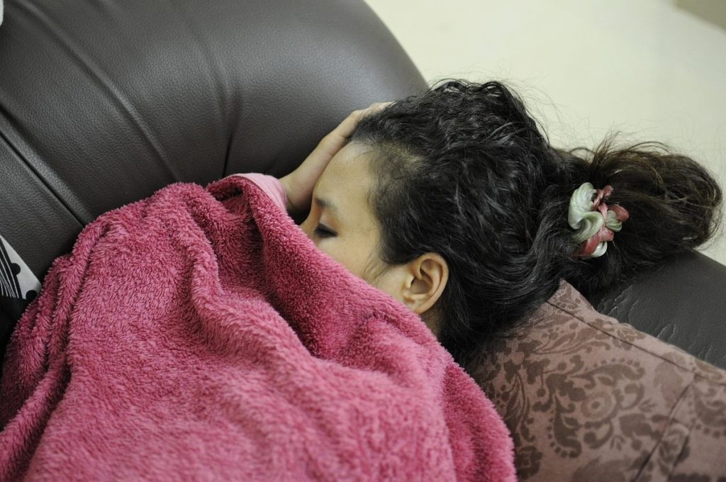Une femme endormie sur un canapé sous une couverture rose