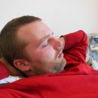 Un homme endormi sur un canapé, la main derrière la tête